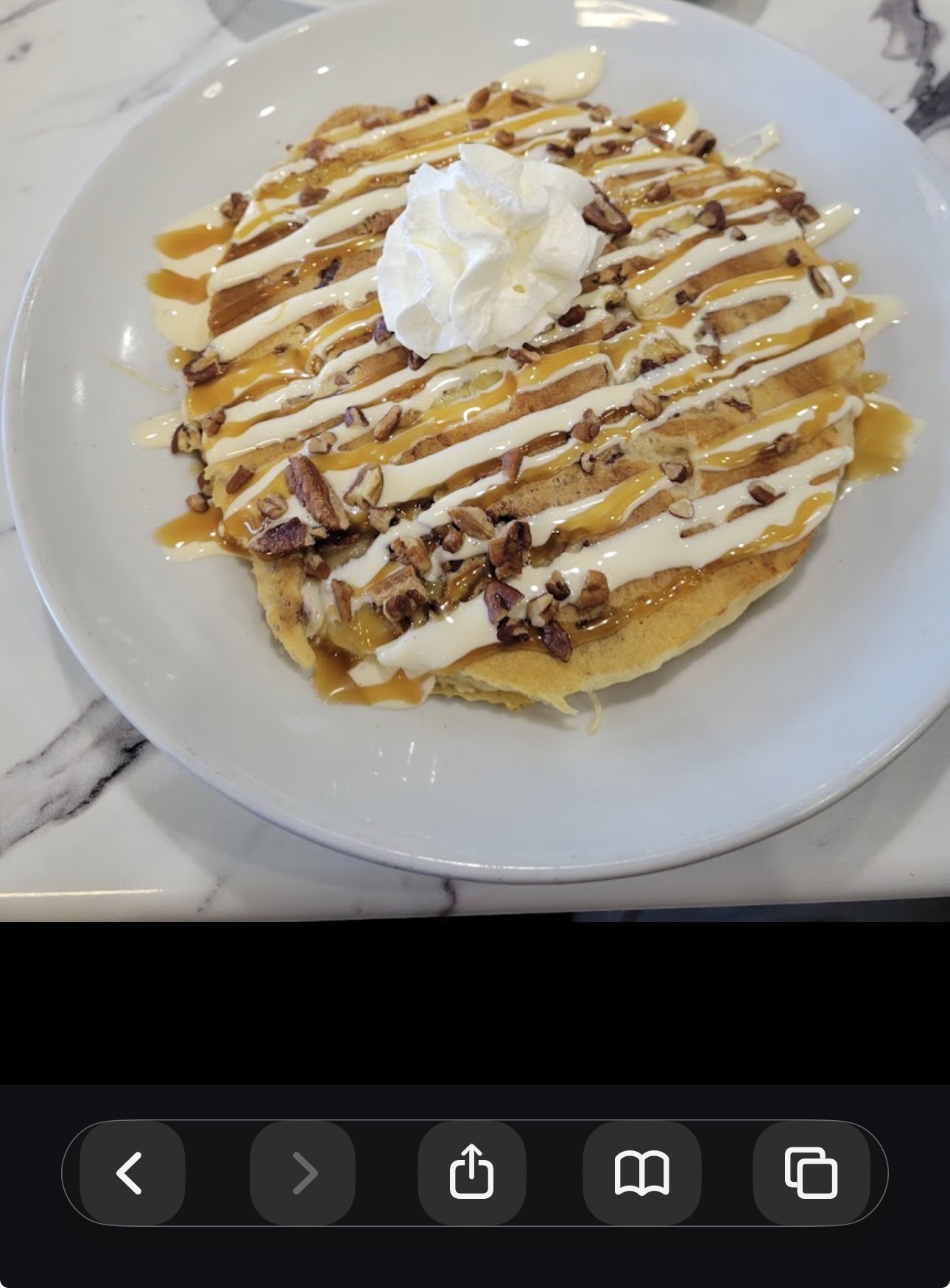 Pancakes topped with drizzles, pecans and whipped cream